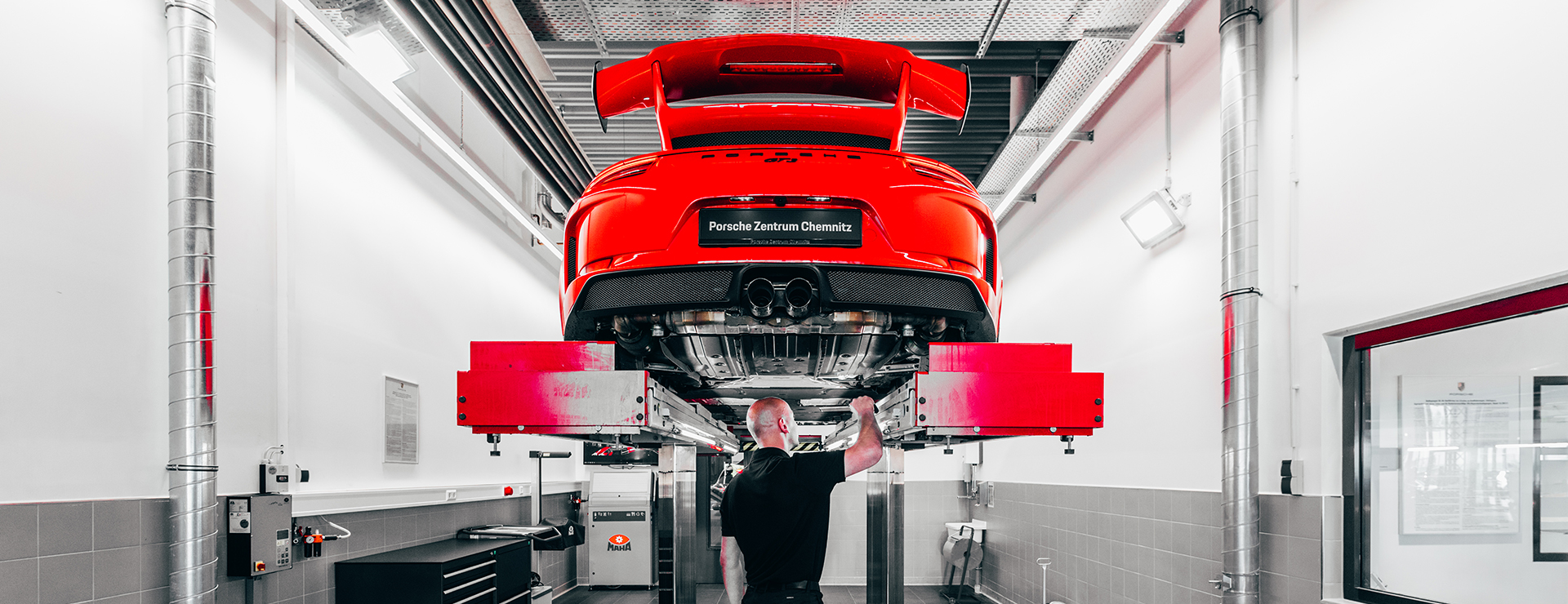 Ein Serviceberater steht mit einem Porsche Sportwagen in der Werkstatt.